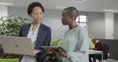 İki Afro-Amerikalı iş kadını ağır çekimde laptoplarını ve tabletlerini kullanarak işi tartışıyor. İş, takım çalışması, kapsayıcılık ve iletişim.