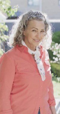 Kameraya bakıp gülümseyen, ağır çekimde mutlu beyaz bir kadının dikey video portresi. Emeklilik, ev hayatı ve yaşam tarzı.