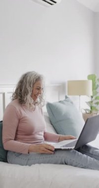 Video görüşmesi için laptop kullanan mutlu, beyaz bir kadının dikey videosu, yavaş çekim. Kaliteli zaman, emeklilik ve teknoloji harcamak.