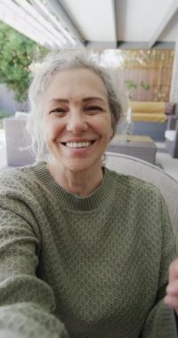 Kafkasyalı yaşlı bir kadının video görüşmesi yaptığı dikey video, yavaş çekim. Emeklilik, ev hayatı, yaşam tarzı, iletişim ve video çağrıları.