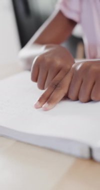 Çift ırklı bir kızın Braille okuduğu dikey video, yavaş çekim. Evde kaliteli zaman geçirmek, ev hayatı, çocukluk, sakatlık ve körlük..
