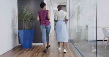 İki Afro-Amerikan iş kadınının ofis koridorunda ağır çekimde yürürken görüntüsü. İş, iş ve iletişim.