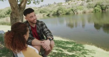 Ormanda gölde bankta oturan mutlu Afrikalı Amerikalı çift, ağır çekimde. Kaliteli zaman geçirmek, yaşam tarzı, doğa, yürüyüş ve kamp..