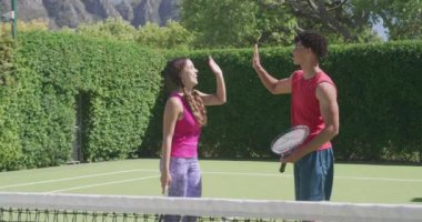 Güneşli bir günde bahçede tenis raketleriyle beşlik çakan mutlu çift. Boş zaman, sağlık ve etkinlik.