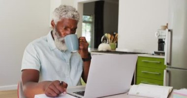 Afro-Amerikan son sınıf öğrencisi kahve içiyor ve dizüstü bilgisayar kullanıyor. Karantina süresince evde tecrit altında kalmak.