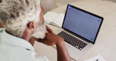 Masadaki Afrikalı Amerikalı kıdemli adam laptopta fotokopi alanı olan bilgisayarla video görüşmesi yapıyor. Karantina süresince evde tecrit altında kalmak.