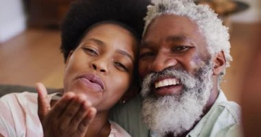 Mutlu Afro-Amerikan çiftler kanepede rahatça oturup video görüşmesi yapıp gülümsüyor ve el sallıyorlar. Karantina süresince evde tecrit altında kalmak.