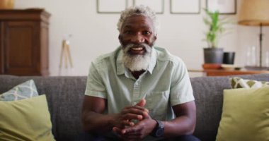 Mutlu Afro-Amerikan son sınıf öğrencisi koltukta oturup video görüşmesi yapıyor, gülümsüyor ve el sallıyor. Karantina süresince evde tecrit altında kalmak.