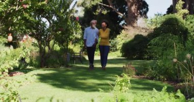 Mutlu Afro-Amerikan çifti el ele tutuşup güneşli bahçede yürüyor. Karantina süresince evde tecrit altında kalmak.