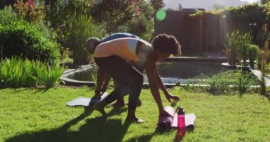 Afrika kökenli Amerikalı son sınıf çifti güneşli bahçede yoga minderlerini sarıyorlar. Karantina süresince evde tecrit altında kalmak.