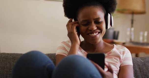 Счастливая Африканская Американка Наушниках Расслабляется Диване Смеясь Над Смартфоном Оставаться — стоковое видео