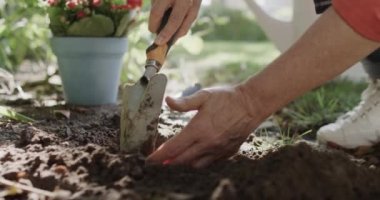 Kafkasyalı bir kadının orta kesiminde bahçede malayla çiçek tarhı hazırlıyor, ağır çekimde. Emeklilik, doğa, bahçıvanlık ve hobiler, değiştirilmemiş model.