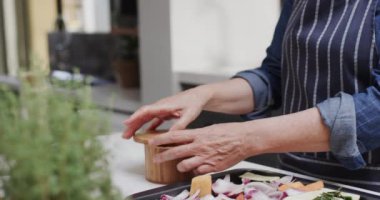 Mutfakta sebze çeşnili kıdemli beyaz kadının orta kesimi, ağır çekim. Kıdemli yaşam tarzı, yemek pişirme ve sağlıklı beslenme, değişmemiş model.