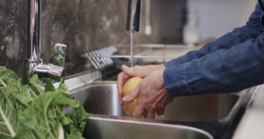 Mutfak lavabosunda sarı biber yıkayan yaşlı, beyaz bir kadının orta bölümü, ağır çekimde. Yaşlı yaşam tarzı, beslenme ve sağlıklı beslenme, değişmemiş model..