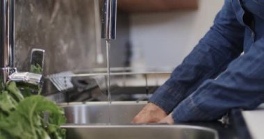 Mutfak lavabosunda sarı biber yıkayan yaşlı, beyaz bir kadının orta bölümü, ağır çekimde. Yaşlı yaşam tarzı, beslenme ve sağlıklı beslenme, değişmemiş model..