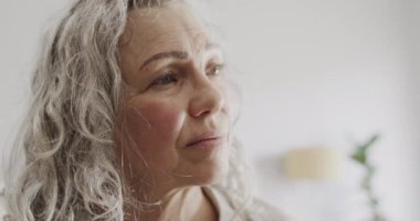 Yaşlı beyaz kadın yatak odasında uzun gri saçlarını hareket ettiriyor, ağır çekimde. Emeklilik, ev hayatı ve yaşam tarzı.
