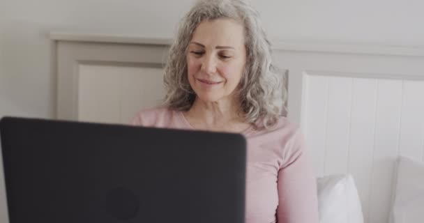Ευτυχισμένη Ηλικιωμένη Λευκή Γυναίκα Που Κάθεται Στο Κρεβάτι Χρησιμοποιώντας Φορητό — Αρχείο Βίντεο