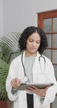 Ağır çekimde tablet kullanan melez bir kadın doktorun dikey portresi. Sağlık personeli, ilaç, iletişim ve sağlık hizmetleri.