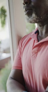 Düşünceli, yaşlı, Afrikalı Amerikalı bir adamın yavaş çekimde çekilmiş dikey videosu. Evde kaliteli zaman geçirmek, emeklilik ve umutsuzluk.