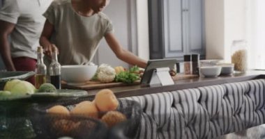 Mutlu Afro-Amerikan çiftler yavaş çekimde ktichen 'de yemek pişirip tablet kullanıyorlar. Evde kaliteli zaman geçirmek, teknoloji ve yiyecek..