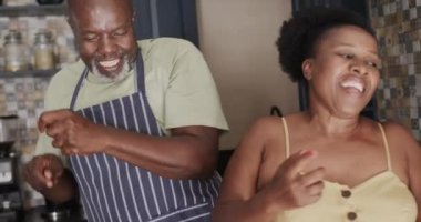 Happy senior african american couple dancing in kitchen in slow motion. Spending quality time at home, retirement and food.