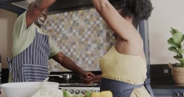 Happy senior african american couple dancing in kitchen in slow motion. Spending quality time at home, retirement and food.