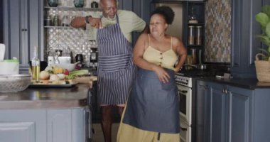 Happy senior african american couple dancing in kitchen in slow motion. Spending quality time at home, retirement and food.