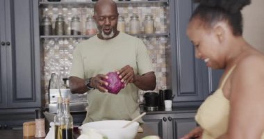 Happy senior african american couple cooking and talking in kitchen in slow motion. Spending quality time at home, retirement and food.