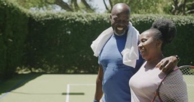 Tenis raketleriyle yürüyen ve tenis kortunda kucaklaşan son sınıf Afro-Amerikan çifti. Emeklilik, aktif yaşam tarzı ve spor.