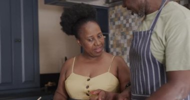 Happy senior african american couple cooking and talking in kitchen in slow motion. Spending quality time at home, retirement and food.