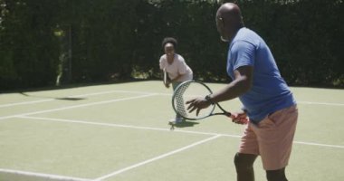 Kıdemli Afro-Amerikan çift tenis kortunda yavaş çekimde oynuyorlar. Emeklilik, aktif yaşam tarzı ve spor.