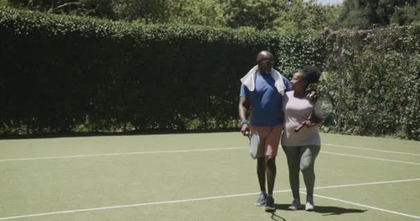 Feliz Casal Afro Americano Sênior Andando Com Raquetes Tênis Abraçando — Vídeo de Stock