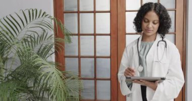 Laboratuvar önlüğü giyen, tablet kullanan, fotokopi çeken, ağır çekimde çift ırklı kadın doktorların portresi. Sağlık personeli, ilaç, iletişim ve sağlık hizmetleri.