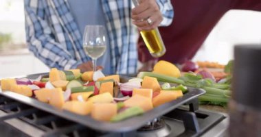 Afrika kökenli Amerikalı eşcinsel erkek çiftin orta kesimi sebzelere zeytinyağı döküyor, ağır çekimde. Yaşam tarzı, ev hayatı ve yemek pişirme..