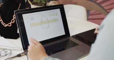 Kuyumcuda ağır çekimde dizüstü bilgisayar kullanan beyaz bir kadın işçi. Mücevher, zanaat, perakende, teknoloji ve küçük işletmeler.