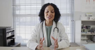 Çift ırklı kadın doktor masada oturuyor ve video görüşmesi yapıyor, ağır çekimde. Sağlık personeli, ilaç, iletişim ve sağlık hizmetleri.