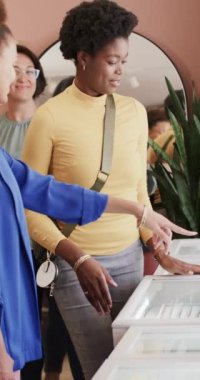 Çeşitli kadın ve satıcının kuyumcuda yavaş çekimde mücevher seçtiği dikey bir video. Mücevher, zanaat, perakende, kapsama ve küçük işletmeler.