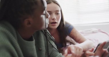 Mutlu genç bayan arkadaşlar yatakta uzanıp, konuşuyorlar ve tablet kullanıyorlar. Arkadaşlık, hafta sonu, iletişim ve yaşam tarzı.