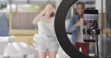 Mutlu genç bayan arkadaşlar dans ediyor ve akıllı telefonlu video blogu yavaş çekimde yapıyor. Ev hayatı, yaşam tarzı, video günlüğü ve teknoloji.