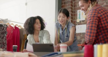 Dizüstü bilgisayar kullanan ve moda tasarım stüdyosundaki işleri yavaş çekimde tartışan mutlu tasarımcılar. Günlük ofis, iş, takım çalışması ve yaratıcı çalışma.