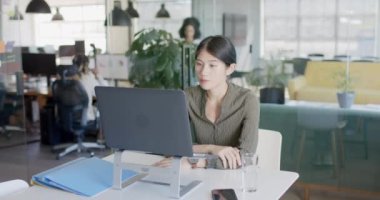 Asyalı sıradan iş kadını ağır çekimde dizüstü bilgisayarla iş görüşmesi yapıyor. Günlük ofis, iş, güven ve iletişim.