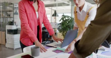 Projeyi tartışan ve masada duran dizüstü bilgisayarları yavaş çekimde kullanan mutlu tasarımcılar. Günlük ofis, iş, takım çalışması ve yaratıcı çalışma.