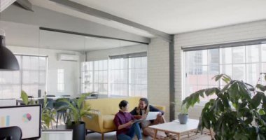 Tablet kullanan ve ofis zemininde ağır çekimde oturup tartışan mutlu yaratıcı meslektaşlar. Günlük ofis, iş, takım çalışması ve yaratıcı çalışma.