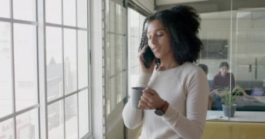 Yaratıcı ofiste akıllı telefondan konuşan mutlu çift ırklı iş kadını, yavaş çekim. Günlük ofis, iş, iletişim ve yaratıcı iş.