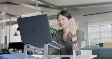 Mutlu Asyalı sıradan iş kadını ağır çekimde dizüstü bilgisayarla iş yerini arıyor. Günlük ofis, iş, güven ve iletişim.