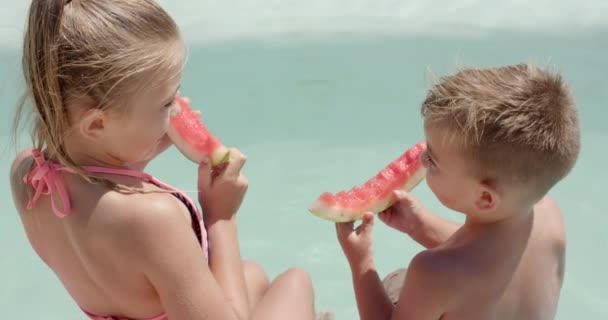 ビーチハウスのプールでスイカを食べている幸せな白人の兄弟 自由時間 夏と子供時代 — ストック動画