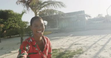 Kırmızı elbiseli mutlu kadın güneşli sahilde dans ediyor ve gülüyor, ağır çekimde. Yaz, dinlenme ve tatiller.