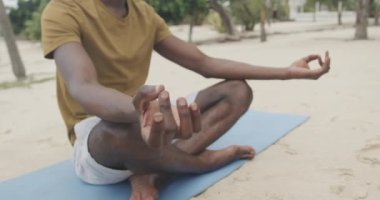 Afrika kökenli Amerikalı bir adamın yoga yapması kumsalda meditasyon yapması, ağır çekim. Yaz, sağlıklı yaşam tarzı, rahatlama ve tatiller.