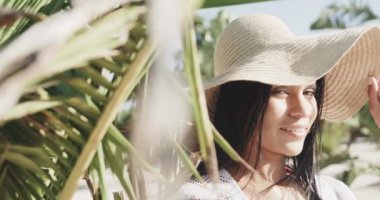 Güneşli sahilde gülümseyen, güneşli şapkalı ve güneşli elbiseli mutlu İspanyol kadın portresi, yavaş çekim. Yaz, dinlenme ve tatiller.