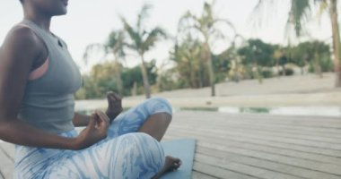 Rıhtımda oturan, fotokopi çeken, ağır çekimde yoga yapan melez kadının alt kesimi. Yaz, rahatlama, sağlıklı yaşam tarzı ve tatiller..